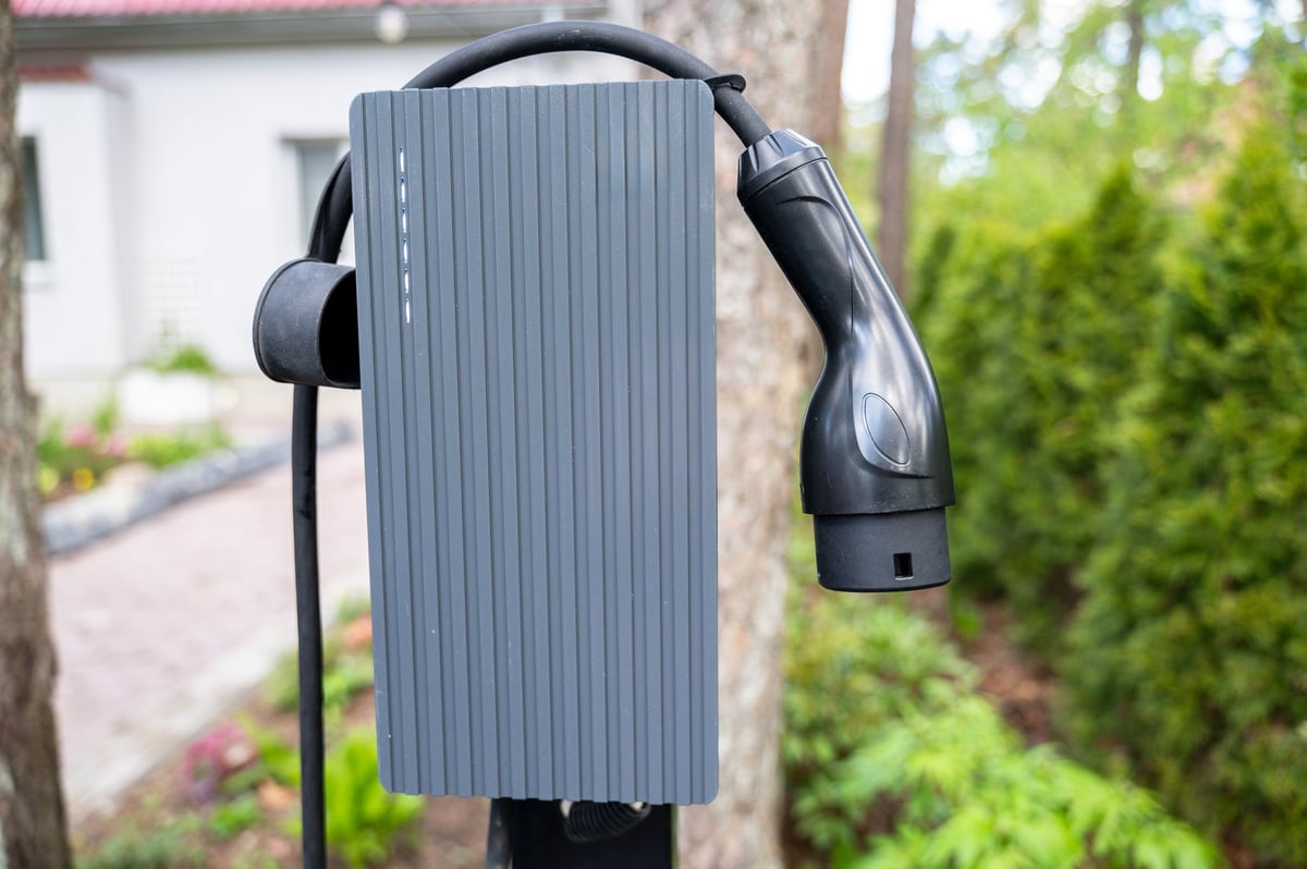 Close-up view of electric vehicle charger mounted outdoors in home driveway. Setup reflects commitment to clean energy and convenient personal charging