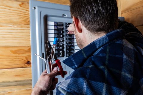 A close-up shot of a technician or handyman using wire strippers to prepare electrical cables for installation in a home circuit breaker box.