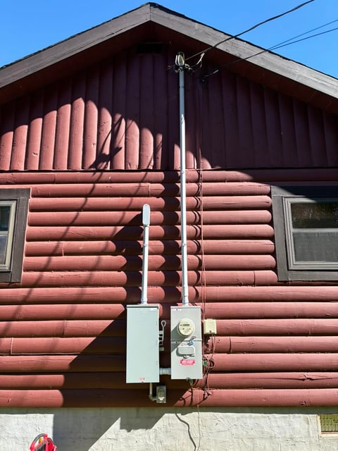 Exterior of red log cabin with electrical meter and antenna mounted on wall under clear blue sky